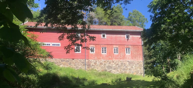 Rød låve med grønne trær i forgunnen, sett fra sør etter istandsetting. Furøya, Agder. Foto.