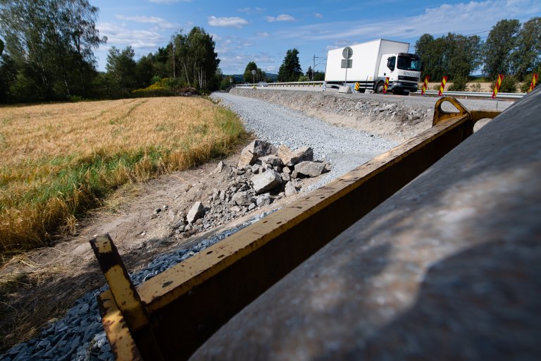 Veiutbygging, lavt kamerastandpunkt. Lastebil på veien, kornåker i venstre billedkant. Pukklag i kanten av veien.